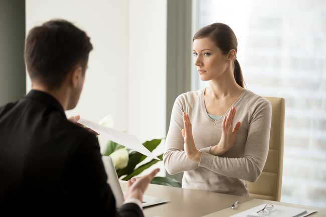 Unconvinced in honesty of business agreement female entrepreneur refusing to sign contact with businessman. Skeptical young woman rejecting job offer when sitting at desk in front of hiring manager