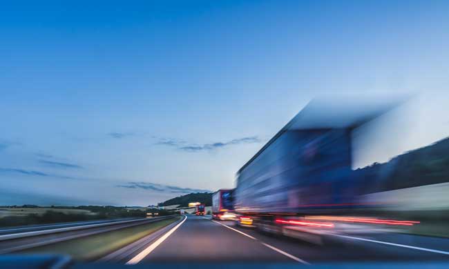 Background photograph of a highway. Truck on a motorway, motion blur, light trails. Evening or night shot of trucks doing logistics and transportation on a highway