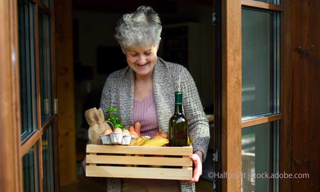 Front view of woman holding food shopping delivery by front door.