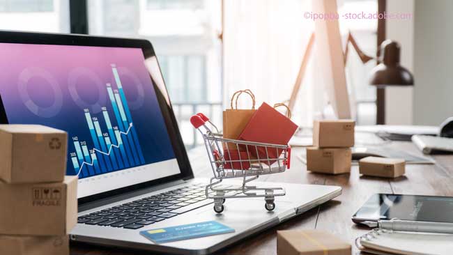 Shopping bags incart and credit card on laptop with paper boxes on table and sales data economic growth graph on screen, buying and selling services online on network, e-commerce concept