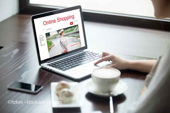 Young woman sitting in cafe with cup of coffee and cakes, working on laptop computer, shopping using online web service