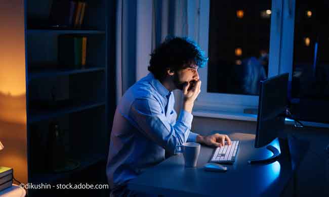 Side view of tired young business man working on computer in home at night