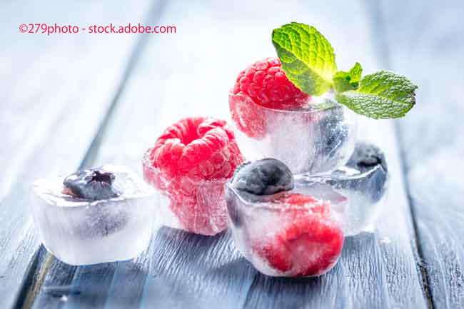 fresh berries with mint in ice cubes on wooden background