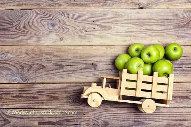 Toy wooden truck with green apples in the back on wooden background