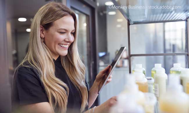 Female Stylist Or Business Owner In Hairdressing Salon Using Digital Tablet To Check Beauty Products