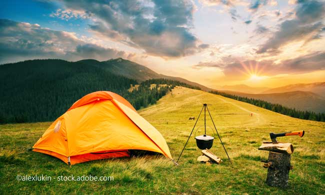 Tourist camp in mountains with tent and cauldron over fire at sunset