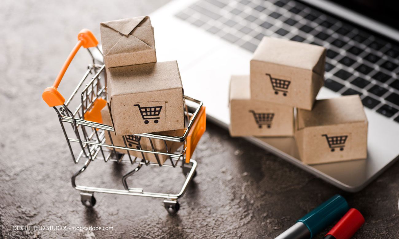 selective focus of toy shopping cart with small carton boxes near laptop, e-commerce concept